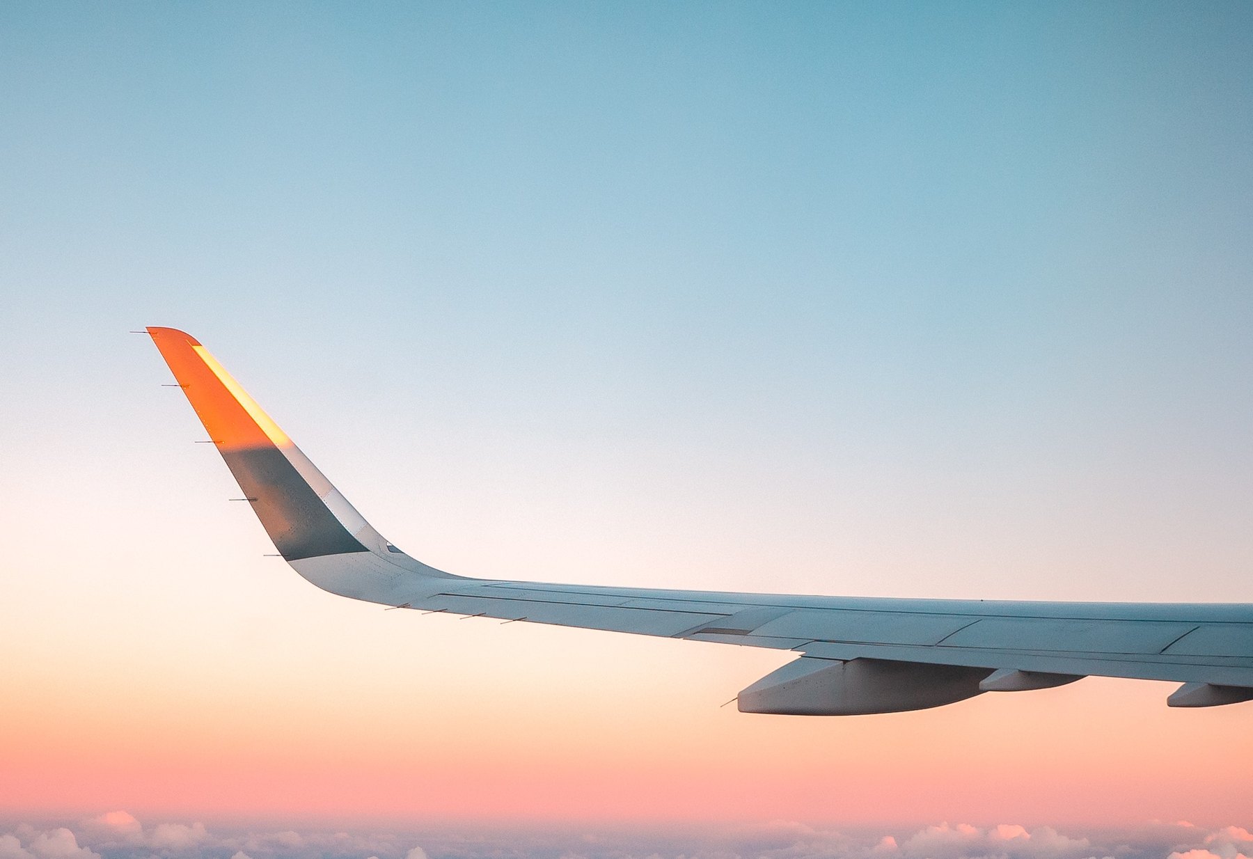 An airliner wingtip above the clouds at sunset