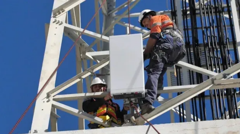 Two technicians in safety harnesses installing equipment on a telecommunications tower